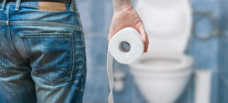 Man facing a toilet holding toilet paper