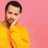 Person sad with hand on face pink background
