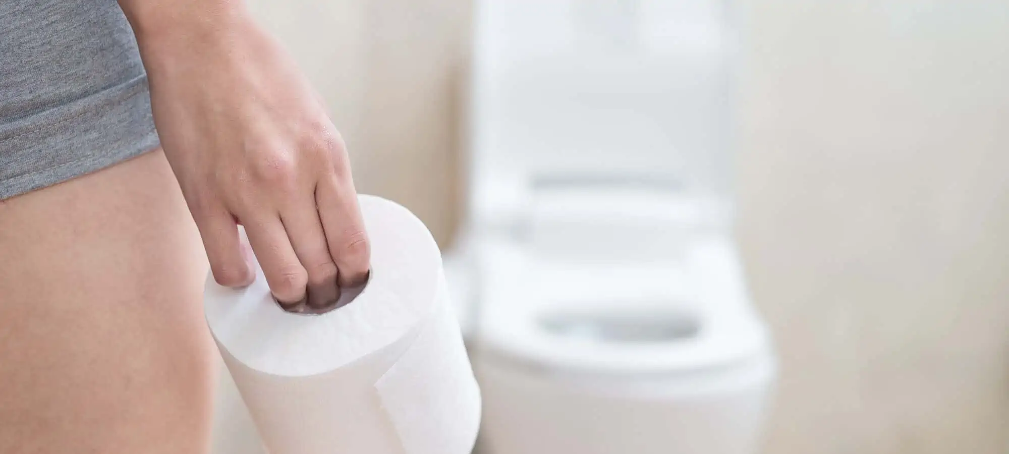 Woman standing in front of a toilet holding toilet pape