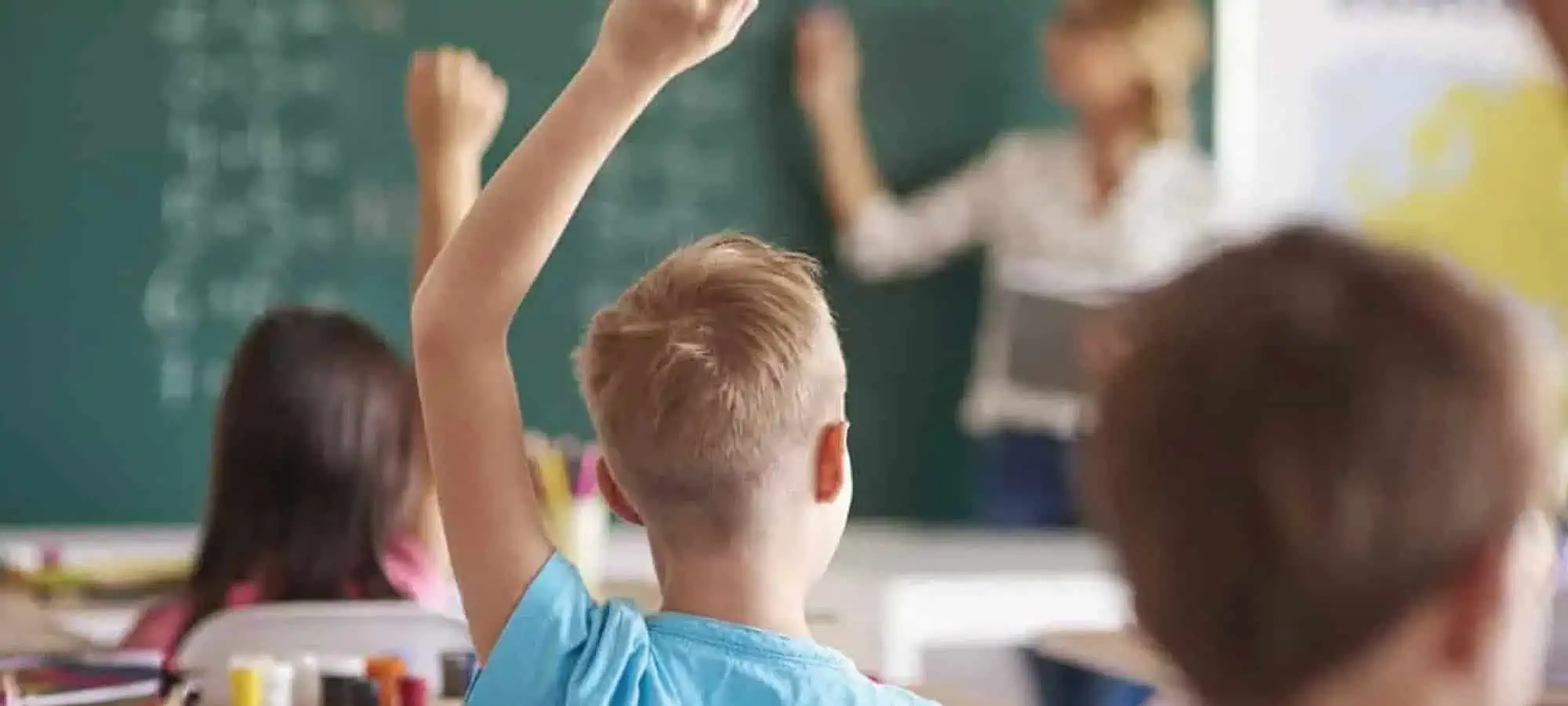 Children in a classroom raising their hands to answer a question