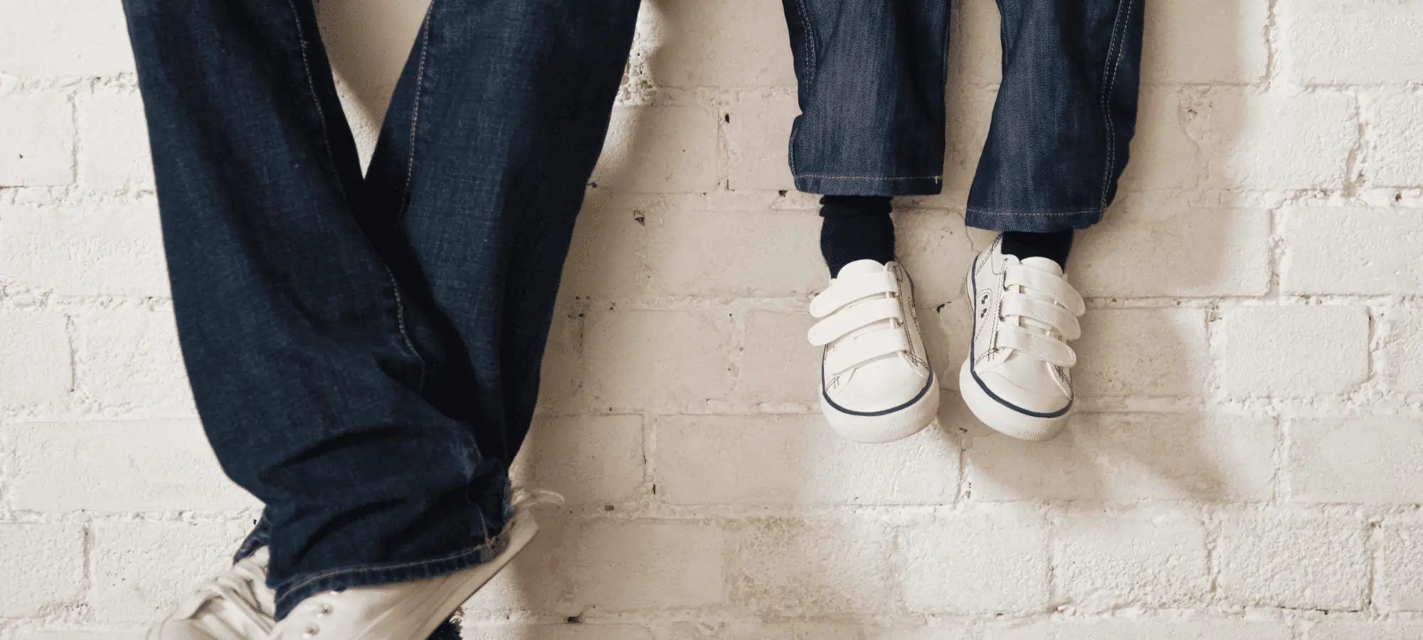 man and child wearing jeans and sneakers with feet dangling