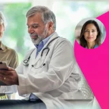 Older female patient sitting beside a male doctor in a white coat with a stethoscope, both smiling while looking at a tablet and discussing bone health during a medical appointment.